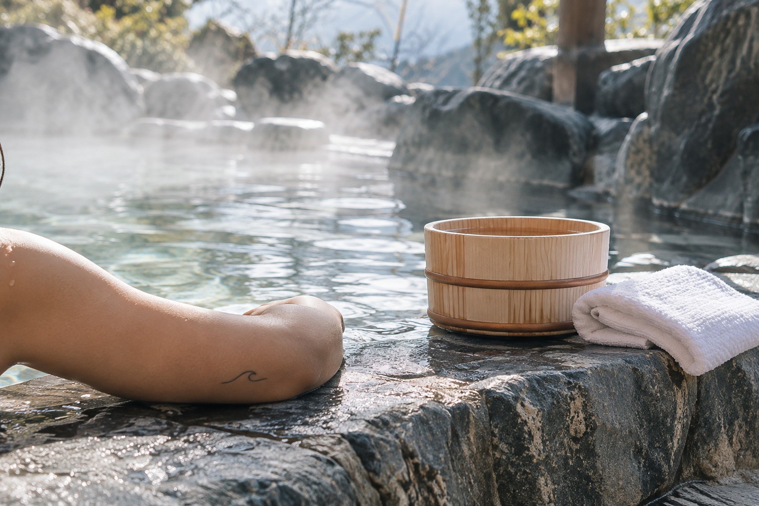 Wooden onsen bucket and towel beside a steaming bath